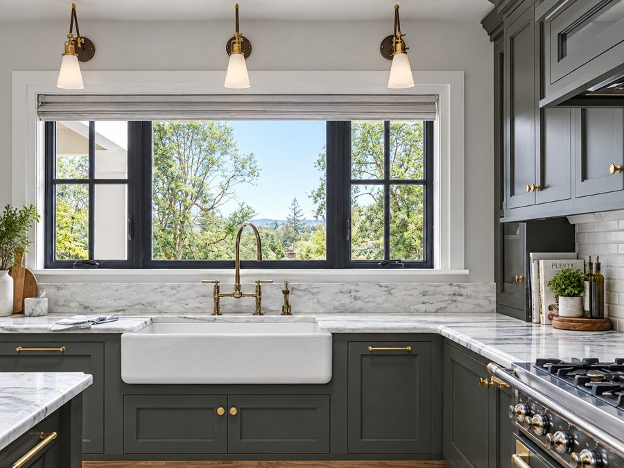 Deep green cabinets with a white apron front sink set into a marble counter under a window