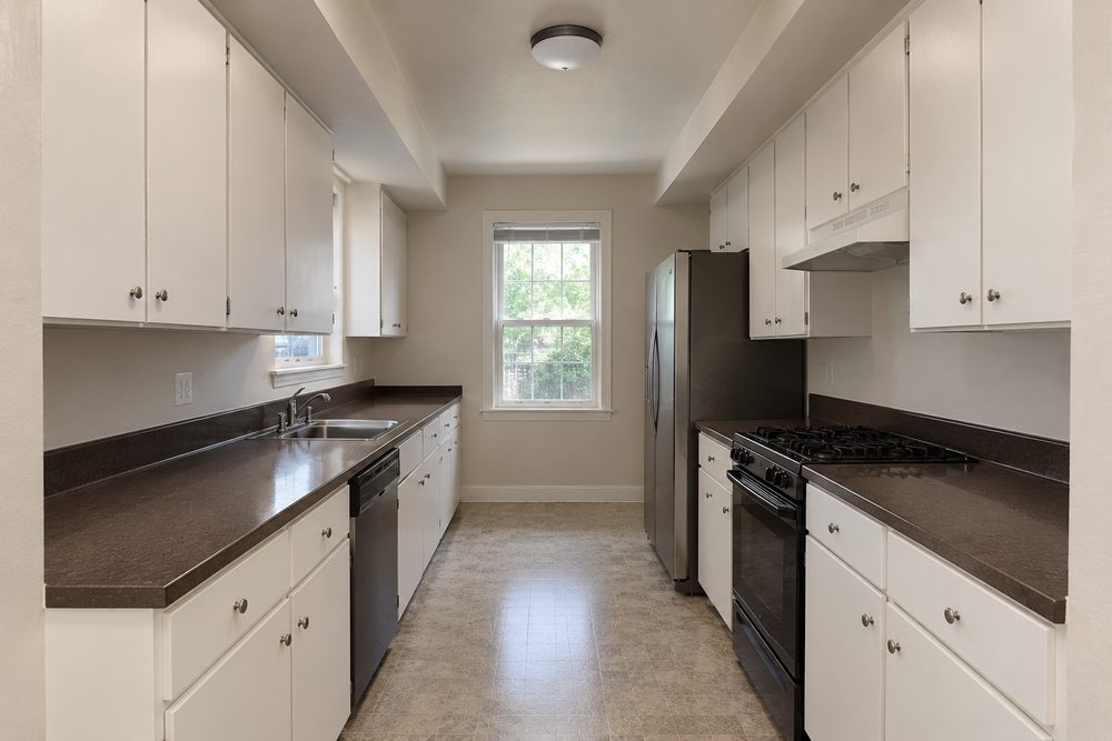 Design rendering of a narrow closed galley with white flat panel doors, dark laminate counters and a boxed soffit above the uppers
